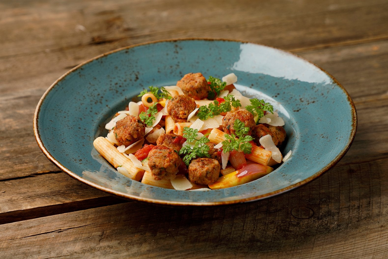 Blå tallrik med pasta och köttbullar som står på ett träbord
